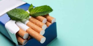 A pack of cigarettes with mint leaves on top against a blue background