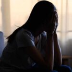 A silhouette of a person sitting with their head in their hands, conveying distress