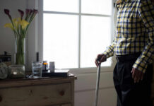 The Untold Story of Strengthspan and Longevity Elderly man standing with a cane next to a table with flowers and medication