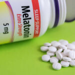 Bottle of melatonin tablets with some pills spilled on a green surface