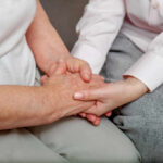An older persons hand being held by a younger persons hand, symbolizing care and connection