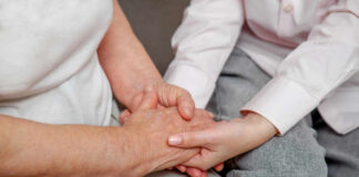 An older persons hand being held by a younger persons hand, symbolizing care and connection