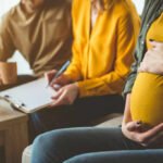 Pregnant woman sitting with two people discussing notes in a cozy living room