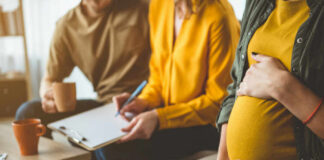 Pregnant woman sitting with two people discussing notes in a cozy living room