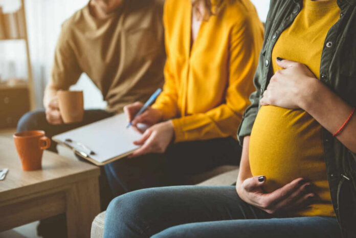 Pregnant woman sitting with two people discussing notes in a cozy living room
