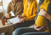 Pregnant woman sitting with two people discussing notes in a cozy living room