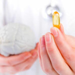 A medical professional holding a brain model in one hand and a yellow supplement capsule in the other