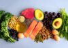 An assortment of healthy foods including fish, nuts, fruits, and vegetables arranged on a light background