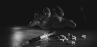 A hand reaching for pills next to a syringe and powder on a table