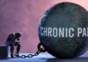 A figure representing chronic pain, sitting beside a large ball labeled 'CHRONIC PAIN' chained to their body