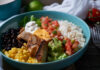 A vibrant bowl filled with grilled chicken, rice, black beans, corn, guacamole, and fresh vegetables