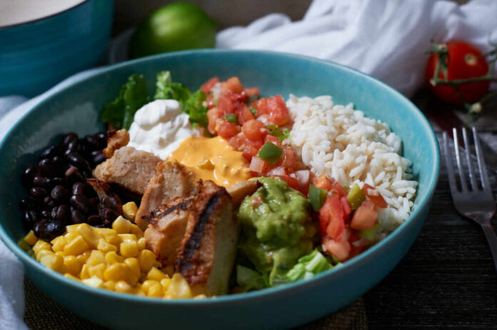 A vibrant bowl filled with grilled chicken, rice, black beans, corn, guacamole, and fresh vegetables