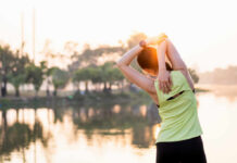 A woman stretching her arms by a lake during sunrise