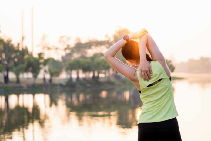 A woman stretching her arms by a lake during sunrise