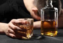 Alcohol Hits Harder Post-30 A person with their head down, holding a glass of whiskey next to a bottle