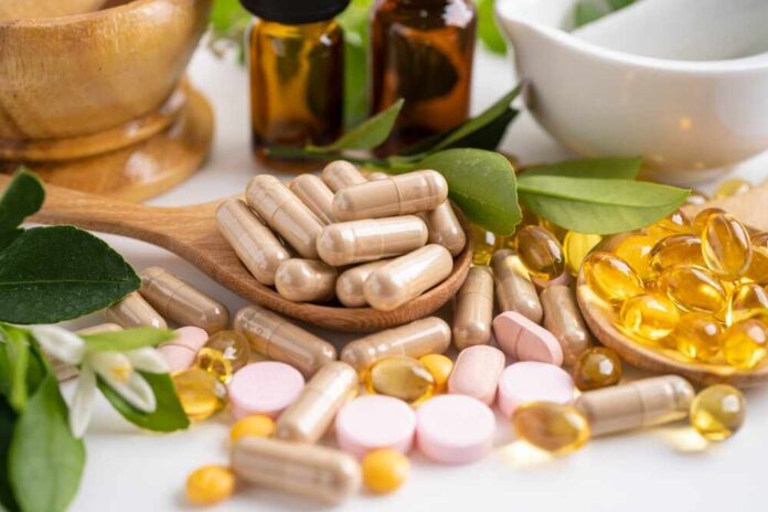Various herbal supplements and vitamins arranged with leaves and a mortar