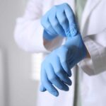 A medical professional putting on blue gloves in a clinical setting