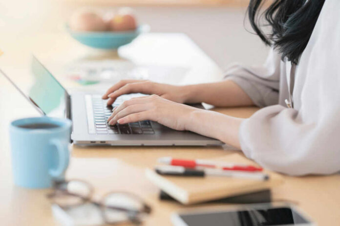 shutterstock1893435241jpg Person typing on a laptop at a home office desk with a coffee cup nearby