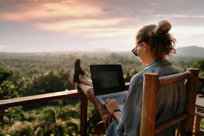 shutterstock_1607004745 Person working on a laptop outdoors with a scenic sunset view