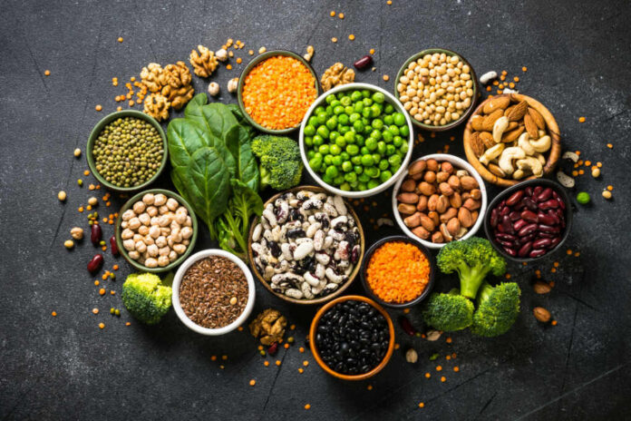 shutterstock_2116460495 An assortment of legumes, nuts, and fresh vegetables arranged in bowls on a dark surface