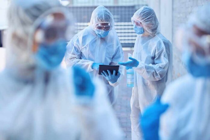 shutterstock_2506350089.jpg Healthcare professionals in protective gear discussing on a tablet