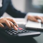 A business professional using a calculator while working on a laptop