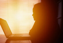 How Indoor Life Quietly Wrecks Your Body Silhouette of a person working on a laptop with sunlight streaming through blinds