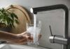 Tap Water Chemical Tied To Dementia A hand holding a glass under a kitchen faucet pouring water