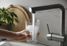 Tap Water Chemical Tied To Dementia A hand holding a glass under a kitchen faucet pouring water