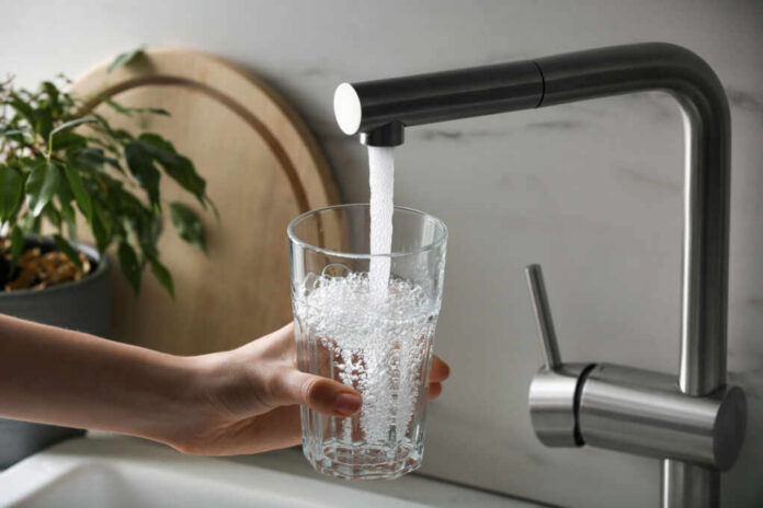 A hand holding a glass under a kitchen faucet pouring water