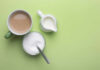 Coffee’s Double-Edged Sword Role In Inflammation A cup of coffee, a bowl of sugar, and a creamer on a green background