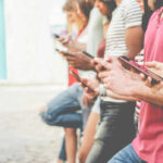 A group of people standing side by side, each using their smartphones in an outdoor setting