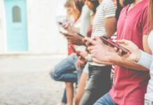 A group of people standing side by side, each using their smartphones in an outdoor setting