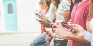 A group of people standing side by side, each using their smartphones in an outdoor setting