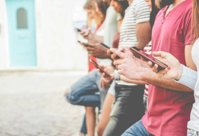 A group of people standing side by side, each using their smartphones in an outdoor setting