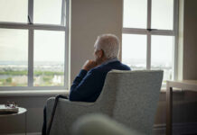 The Overlooked Clock Driving Dementia Elderly man sitting in a chair, looking out a window with a thoughtful expression