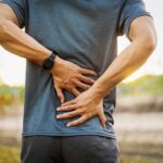 How To Tell The Difference Between Muscle Soreness And Real Injury Person holding lower back in pain outdoors
