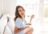 Woman sitting on a couch eating a bowl of fruit salad