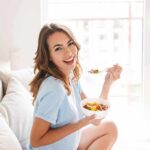 Woman sitting on a couch eating a bowl of fruit salad