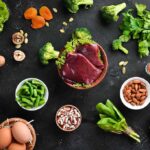 Raw liver with assorted healthy foods on dark surface