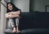Woman sitting on a couch hugging her knees by a window