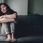 Why Isolation and Loneliness are Dangerous Woman sitting on a couch hugging her knees by a window