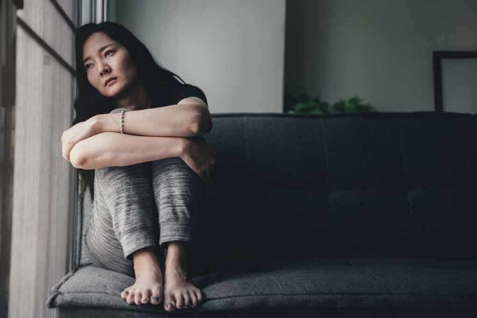 Woman sitting on a couch hugging her knees by a window