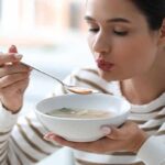 Woman blowing on a spoonful of hot soup