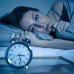 Dangers of Using Cannabis and Alcohol Before Sleep Woman lying awake in bed beside an alarm clock