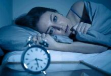 Dangers of Using Cannabis and Alcohol Before Sleep Woman lying awake in bed beside an alarm clock