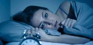 Woman lying awake in bed beside an alarm clock