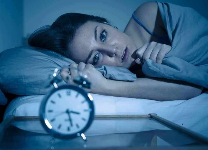 1783889734358-5sk8rq-shutterstock-1452406124 Woman lying awake in bed beside an alarm clock