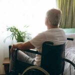 older man in a wheelchair looking out a bright window