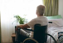 older man in a wheelchair looking out a bright window